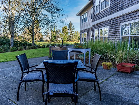 A patio setup with a table and chairs in a sunny backyard, adjacent to a house.