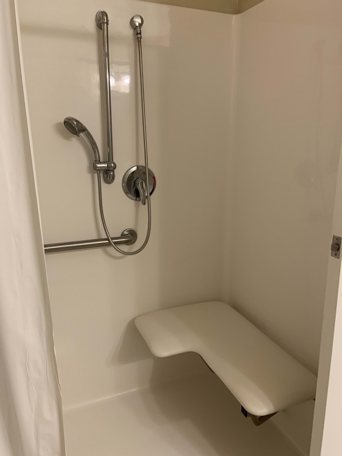 An accessible shower with a handheld showerhead, grab bar, and built-in bench.