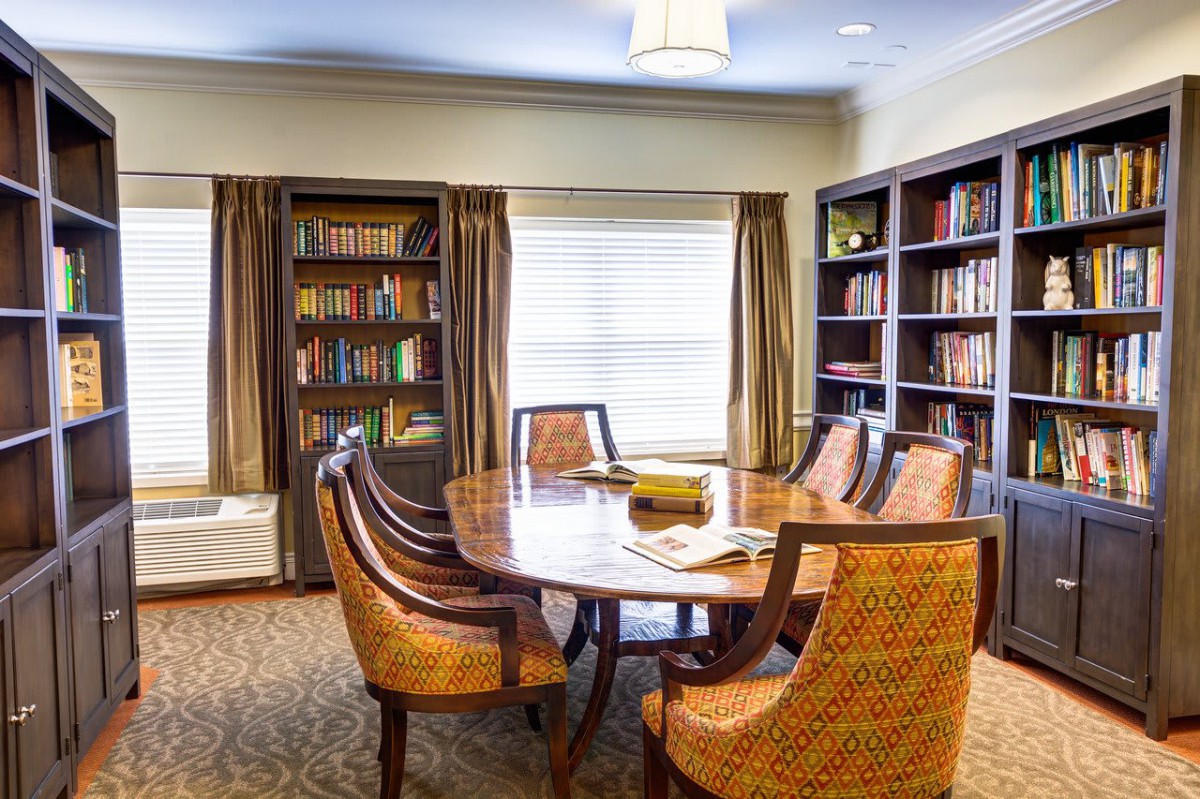 A cozy study room with a large meeting table surrounded by chairs and lined with bookshelves.