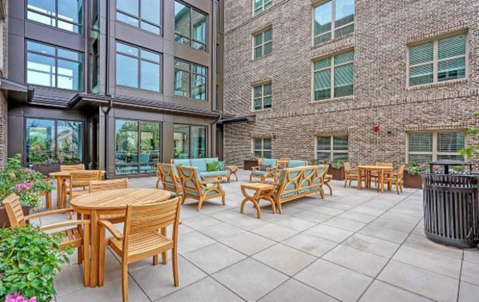 A modern outdoor patio area with wooden furniture surrounded by a building exterior.