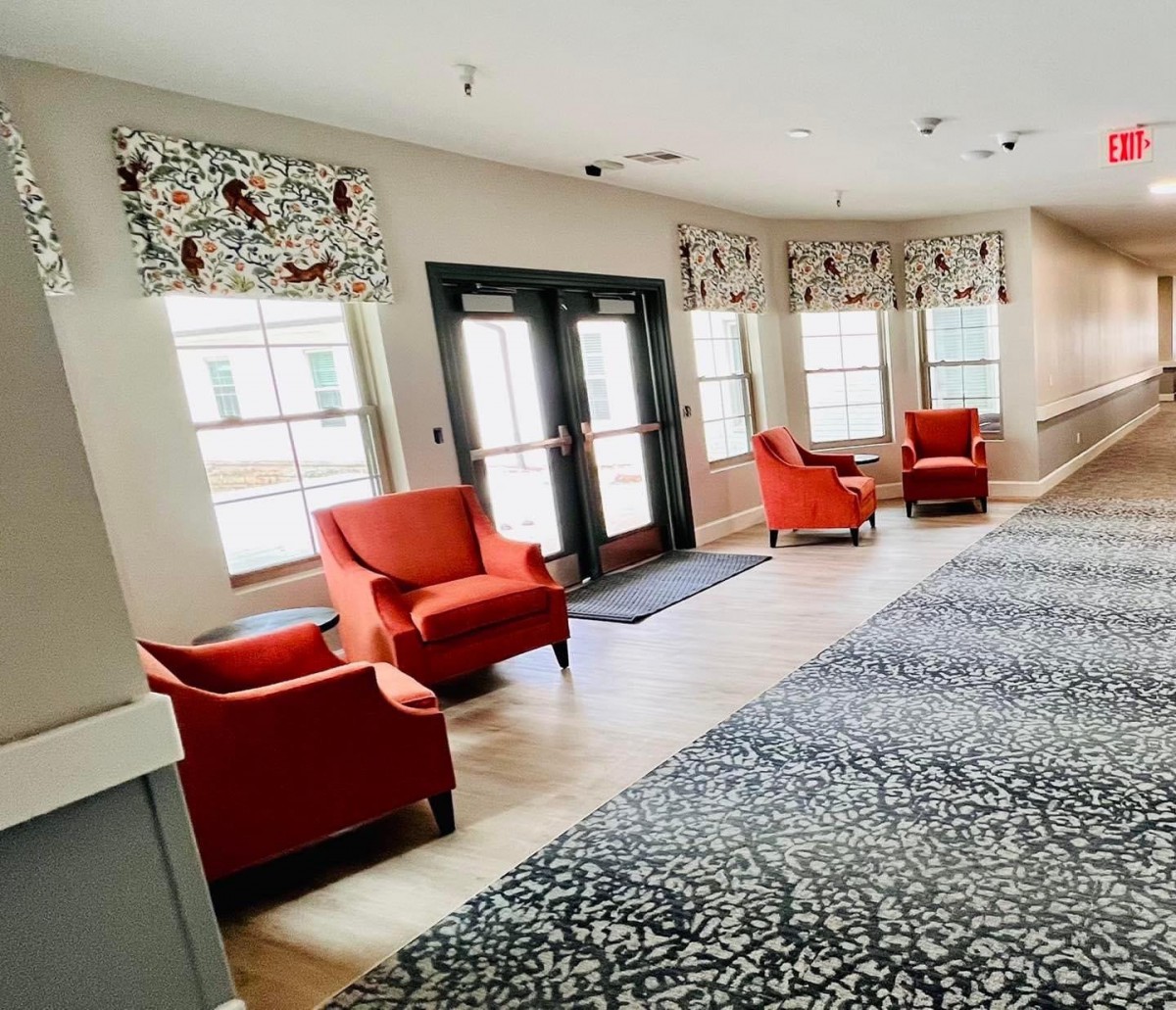 A cozy lobby area featuring vibrant red chairs, large windows with patterned curtains, and a textured carpet.