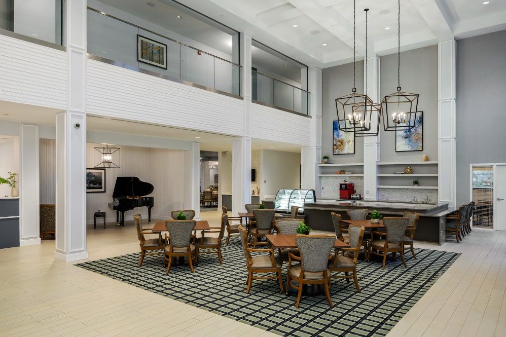 A modern lobby with a dining area featuring tables and chairs, a piano, and stylish pendant lighting.