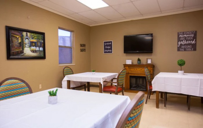 A small dining area with tables covered in white tablecloths, decorated with artwork and a wall-mounted television.