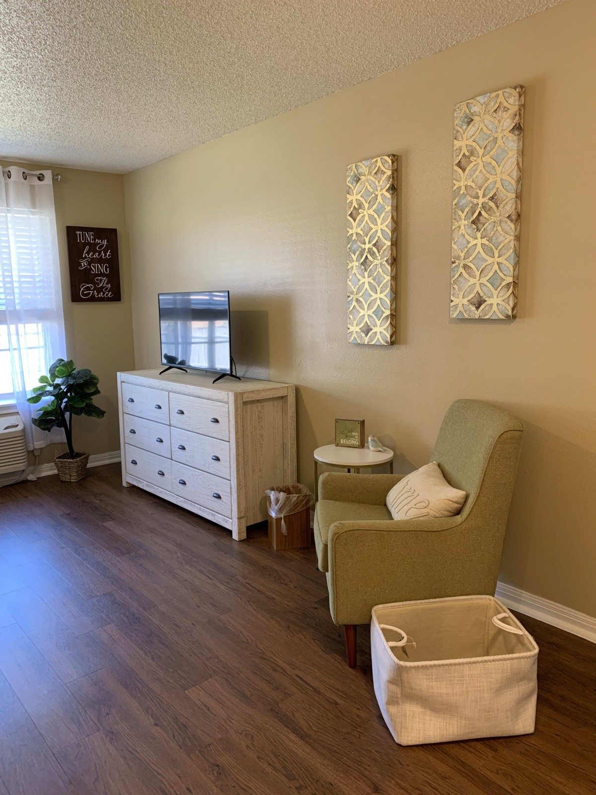 A cozy living room with an armchair, dresser, TV, and decorative elements on the wall.