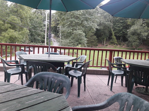 A view of an outdoor dining area with tables and chairs under green umbrellas, surrounded by nature.