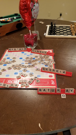 A game of Scrabble in progress with colorful letter tiles and a refreshing drink.