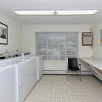 A clean and organized laundry room with washing machines, a table, and a chair.