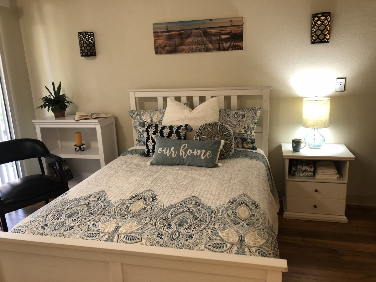 A cozy bedroom with a neatly made bed, featuring decorative pillows and a patterned quilt, accompanied by a lamp on the nightstand.