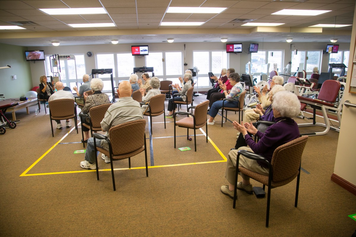 A group of elderly individuals seated in a room for a community meeting.
