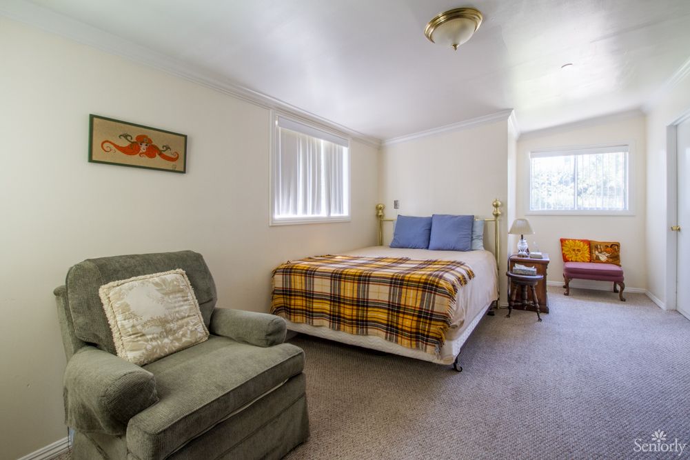 A cozy bedroom with a bed, chair, and natural light filtering through the windows.