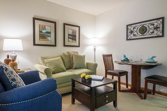 A cozy living room with a green sofa, blue armchair, and wall art.