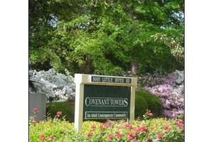 A sign reading 'Covenant Woods' surrounded by a lush garden with colorful flowers and trees.