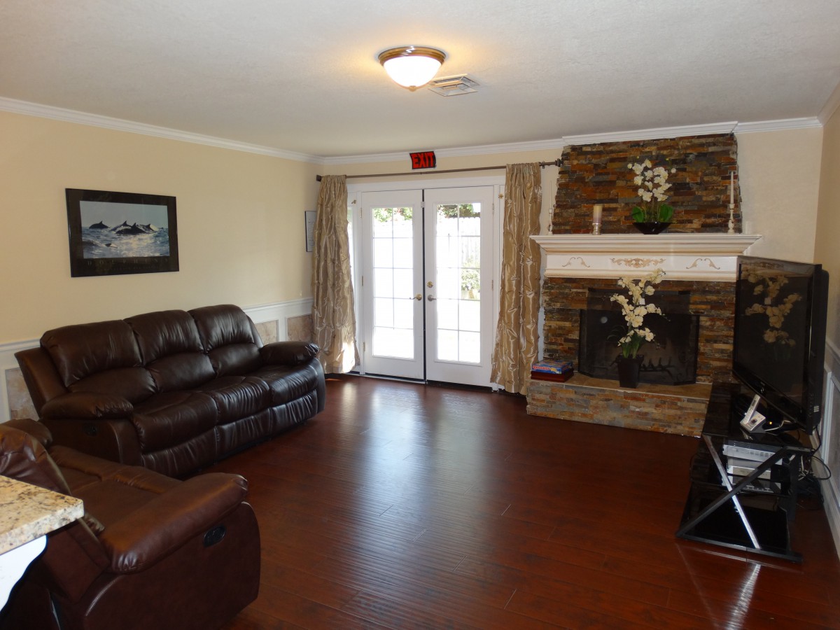 A cozy living room featuring a leather sofa, stone fireplace, and hardwood flooring with natural light from French doors.