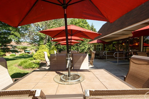 A serene outdoor patio with red umbrellas providing shade, surrounded by lush greenery.