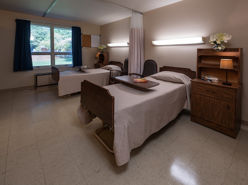 A patient room in a hospital featuring two beds and natural lighting.