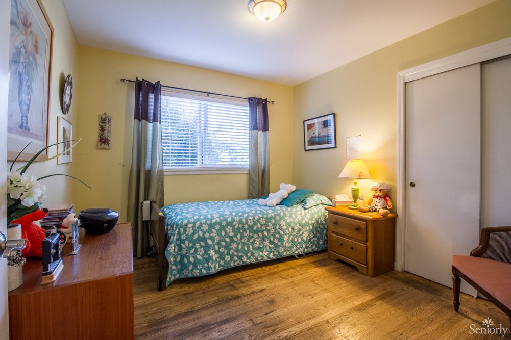 A cozy bedroom with a bed, wooden flooring, and a warm light from a lamp.