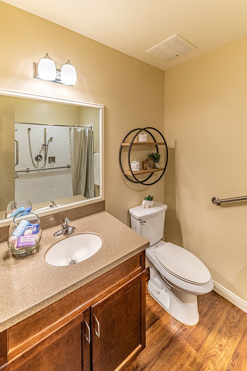 A clean and well-organized bathroom with a mirror, sink, toilet, and shower area.