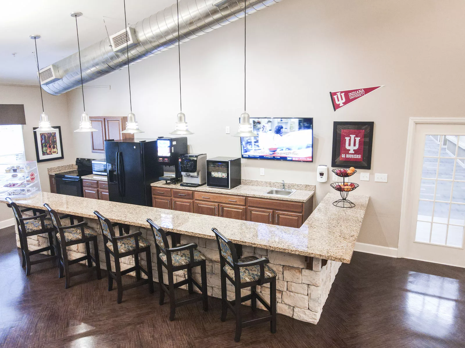 A modern kitchen with a bar counter, equipped with seating and decorated with university memorabilia.