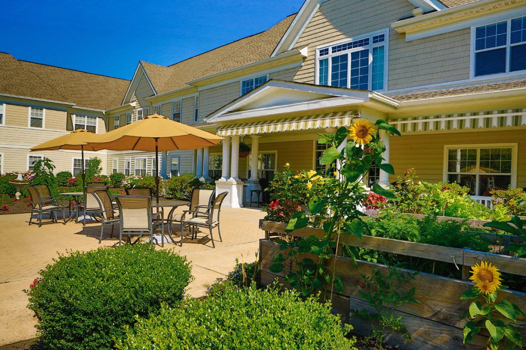 A beautiful garden patio with outdoor furniture and a sunflower, set against a charming residential building on a sunny day.
