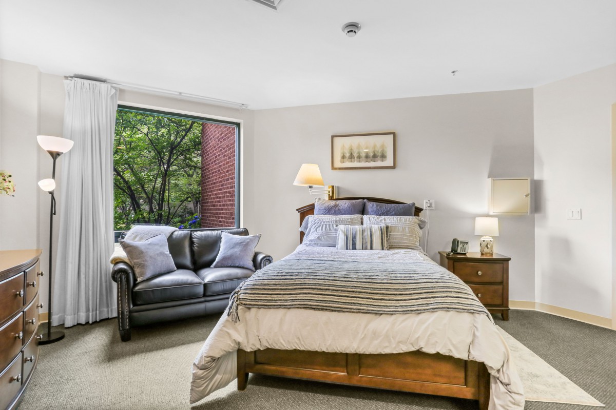 A cozy bedroom with a double bed, sofa, and a large window providing natural light.