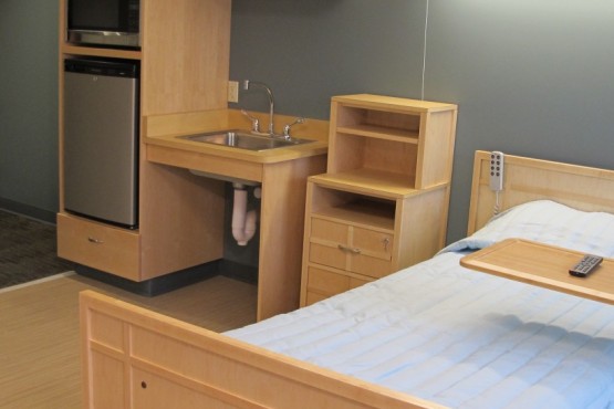 A simple dorm room setup featuring a wooden bed, sink, and storage drawers.