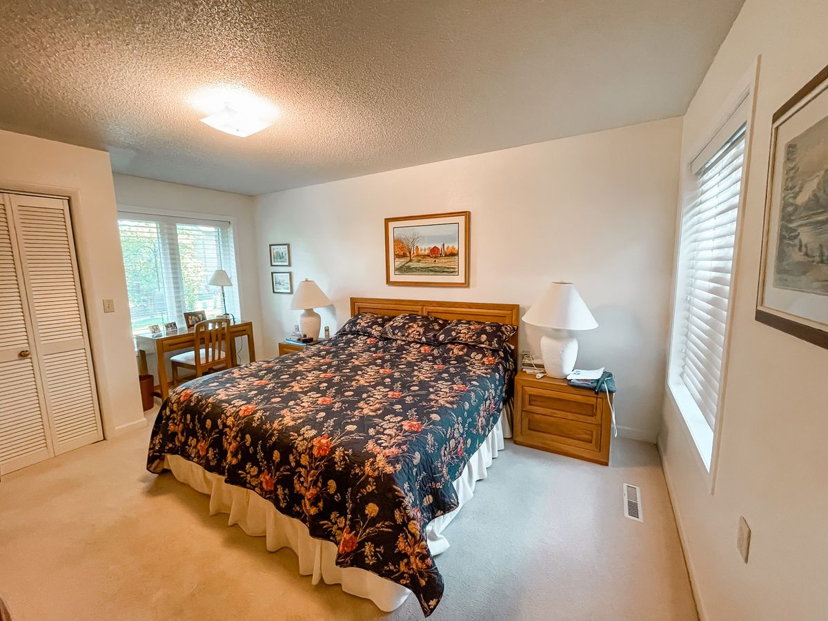 A cozy bedroom with a large bed, nightstands, and lamps, featuring a floral bedspread and a painting above the headboard.