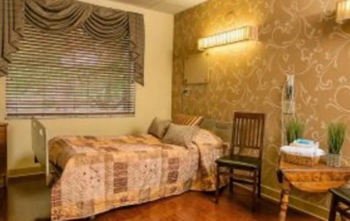 Cozy bedroom with a single bed, decorated with patterned wallpaper and a wooden chair.