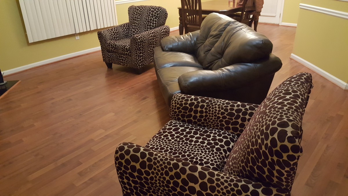 A stylish living room featuring a black leather sofa and leopard print armchairs on a wooden floor.