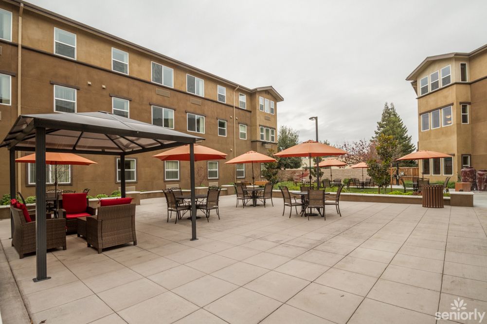 A spacious outdoor patio with tables, chairs, and umbrellas adjacent to a building.