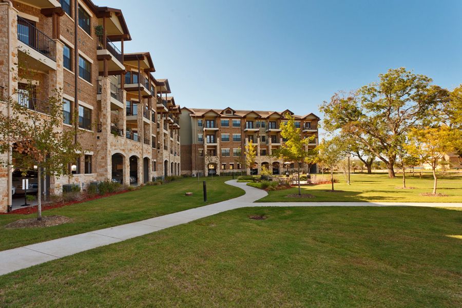 A modern apartment building with a landscaped lawn and pathway under a clear blue sky.