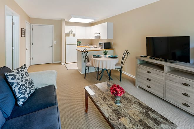 A cozy living area with an open-plan kitchen, featuring a television, sofa, and dining table.