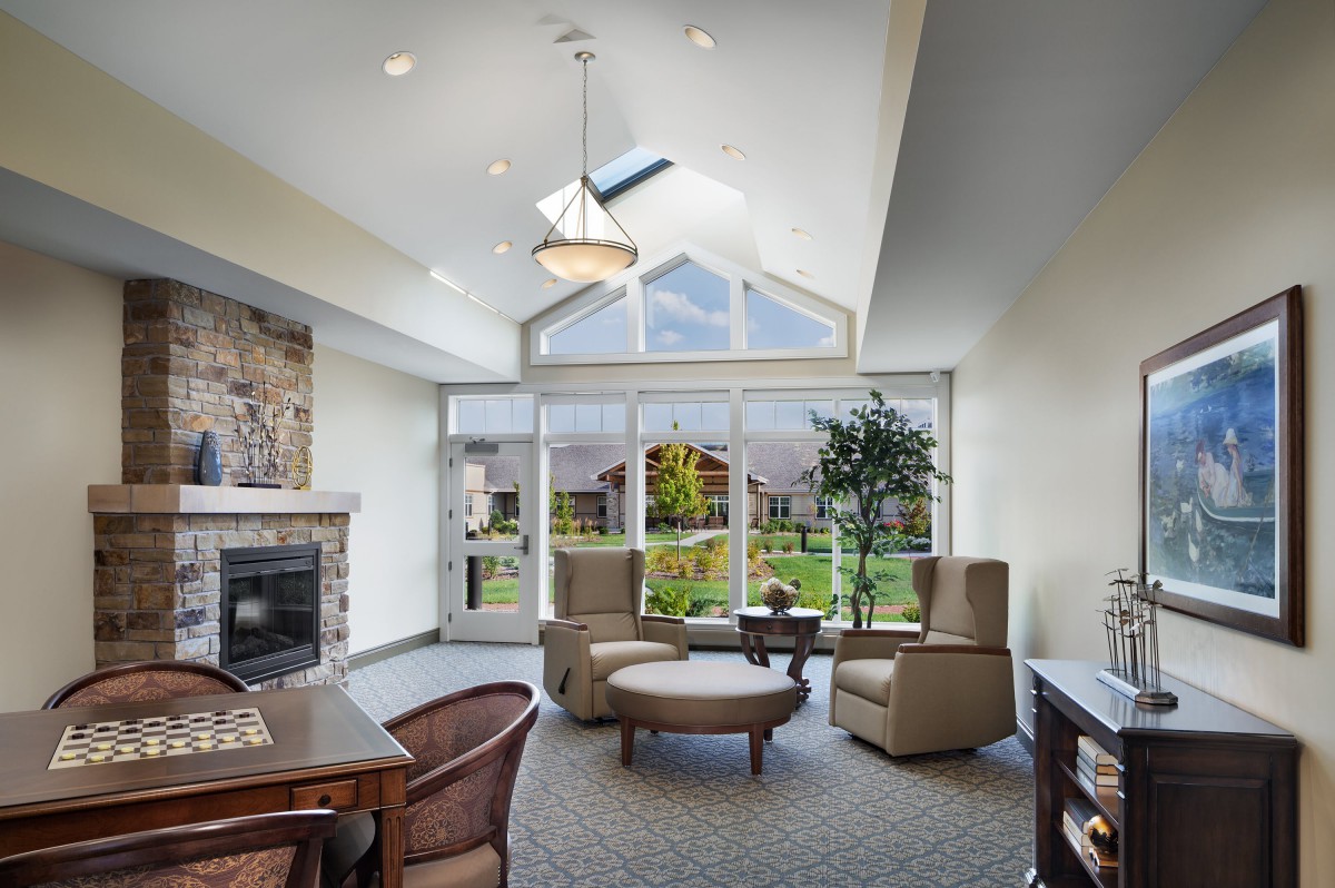 A modern and cozy living room with large windows, a skylight, and comfortable seating around a fireplace.