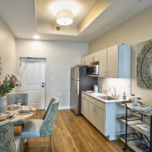 A modern apartment kitchen and dining area with sleek furnishings and wooden flooring.