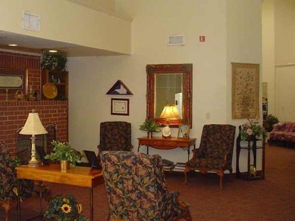 A cozy living room setting with comfortable chairs, a lamp on a side table, and decorative plants.