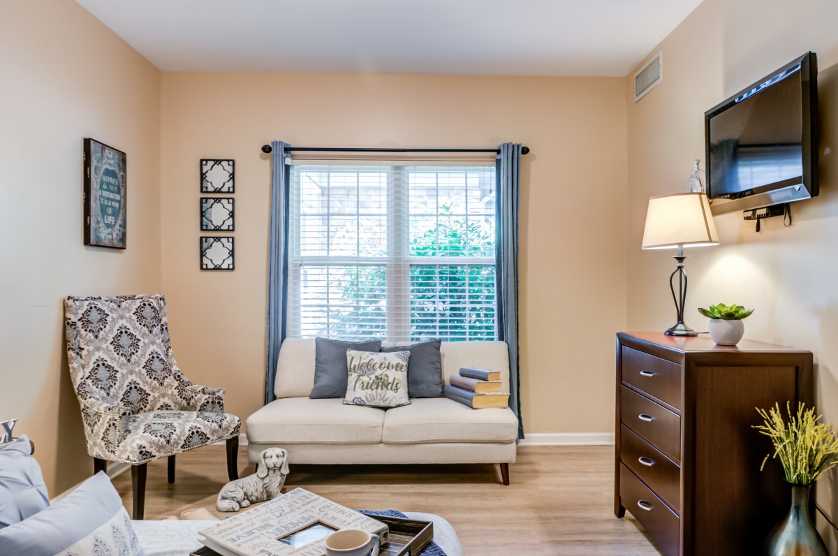 A cozy living room with a sofa, patterned chair, and standing lamp by the window.