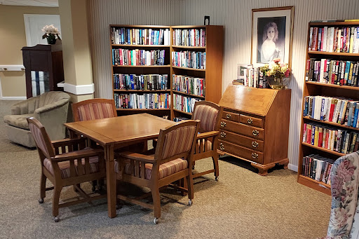 A cozy reading nook with a wooden table and chairs beside a bookshelf filled with books.