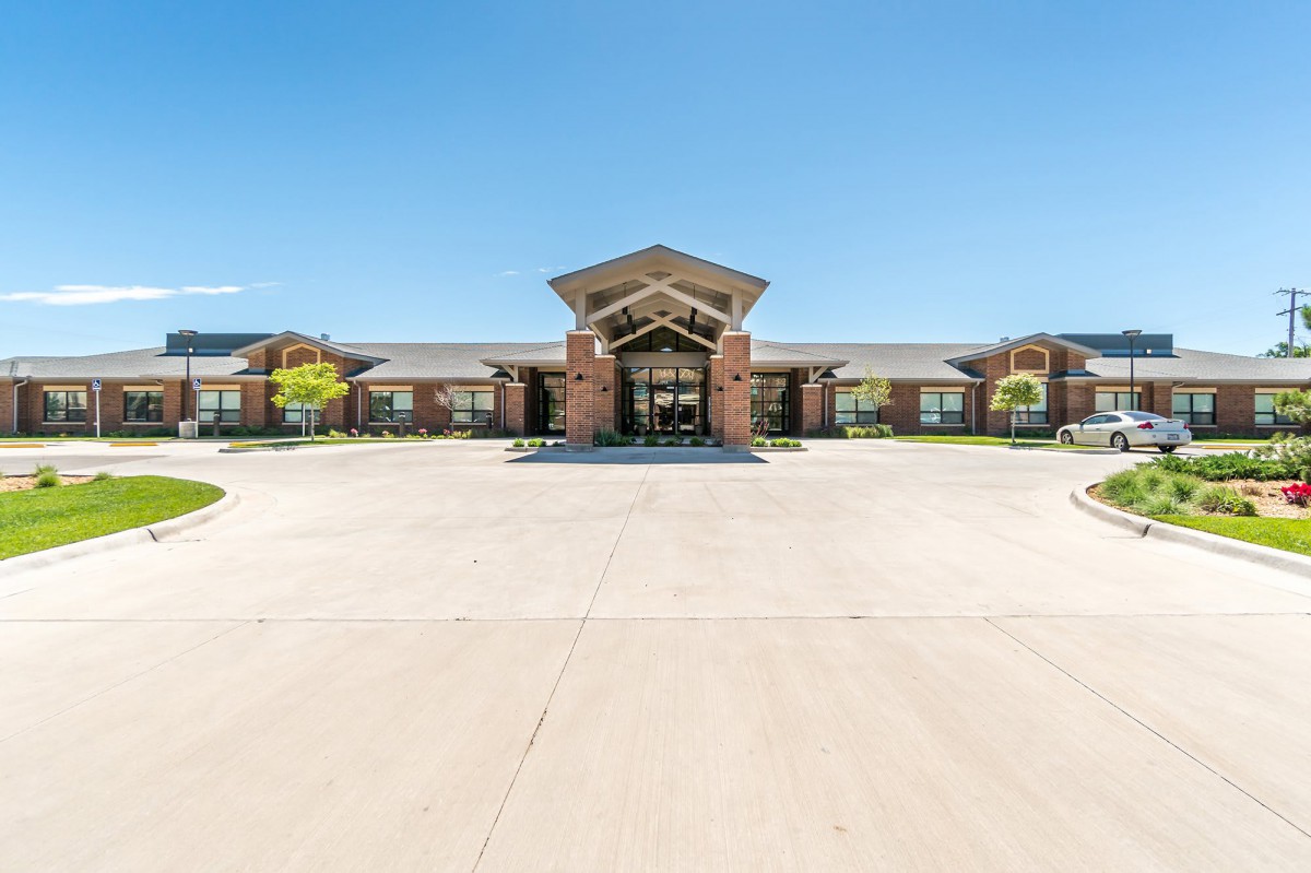 A wide view of a brick building with a prominent entrance and a large driveway on a clear, sunny day.