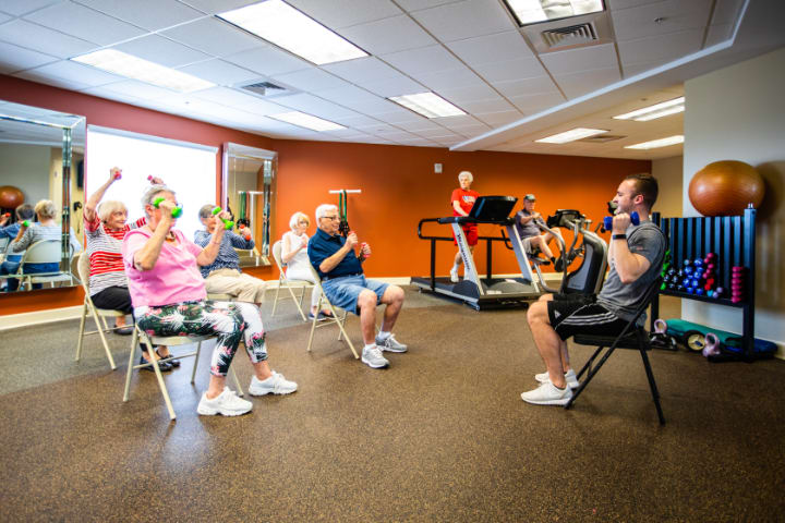 A group of senior citizens participating in a seated exercise class indoors.