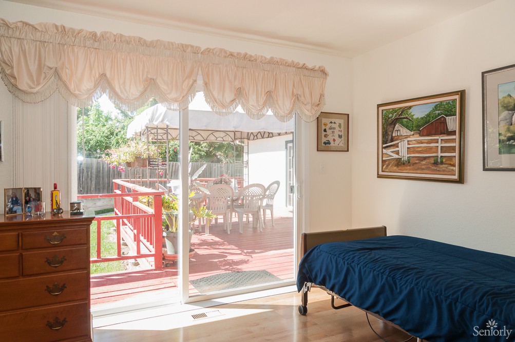 A cozy bedroom with a single bed, featuring a sliding glass door that opens to a sunlit deck with outdoor furniture.