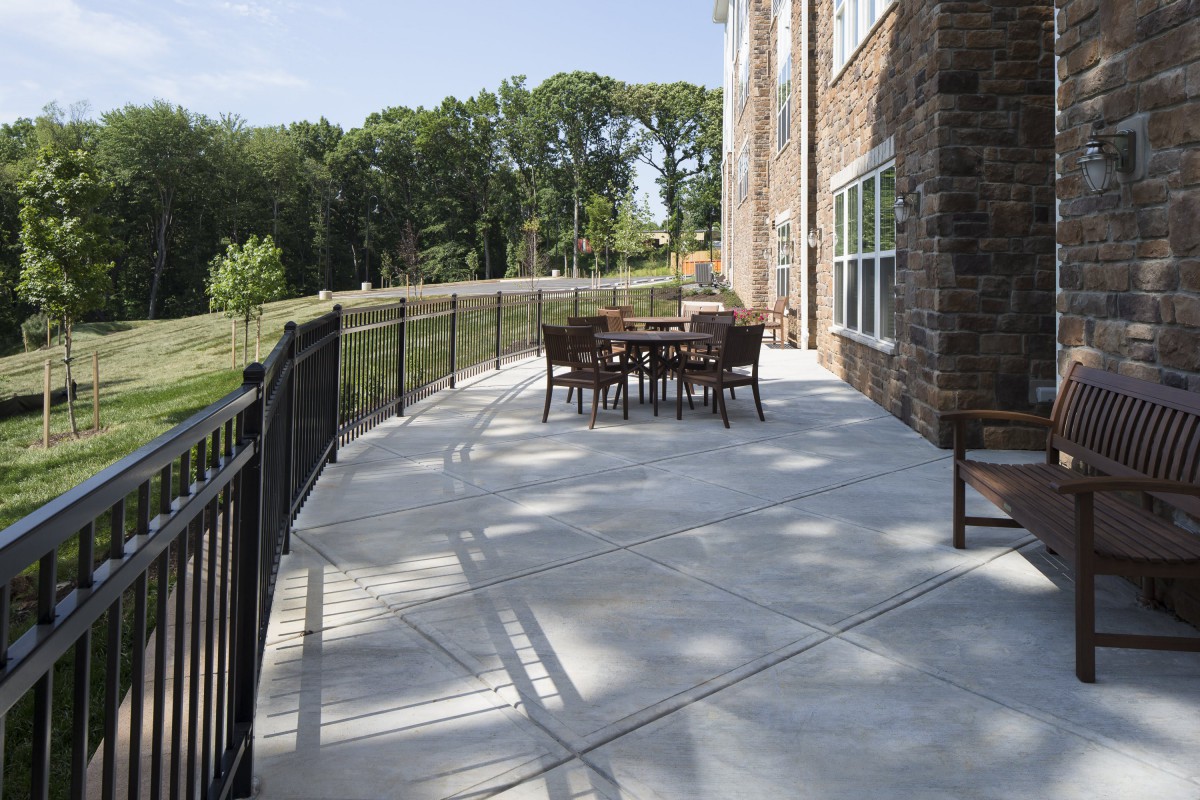 A sunny outdoor patio with a table and chairs, surrounded by a railing and trees.
