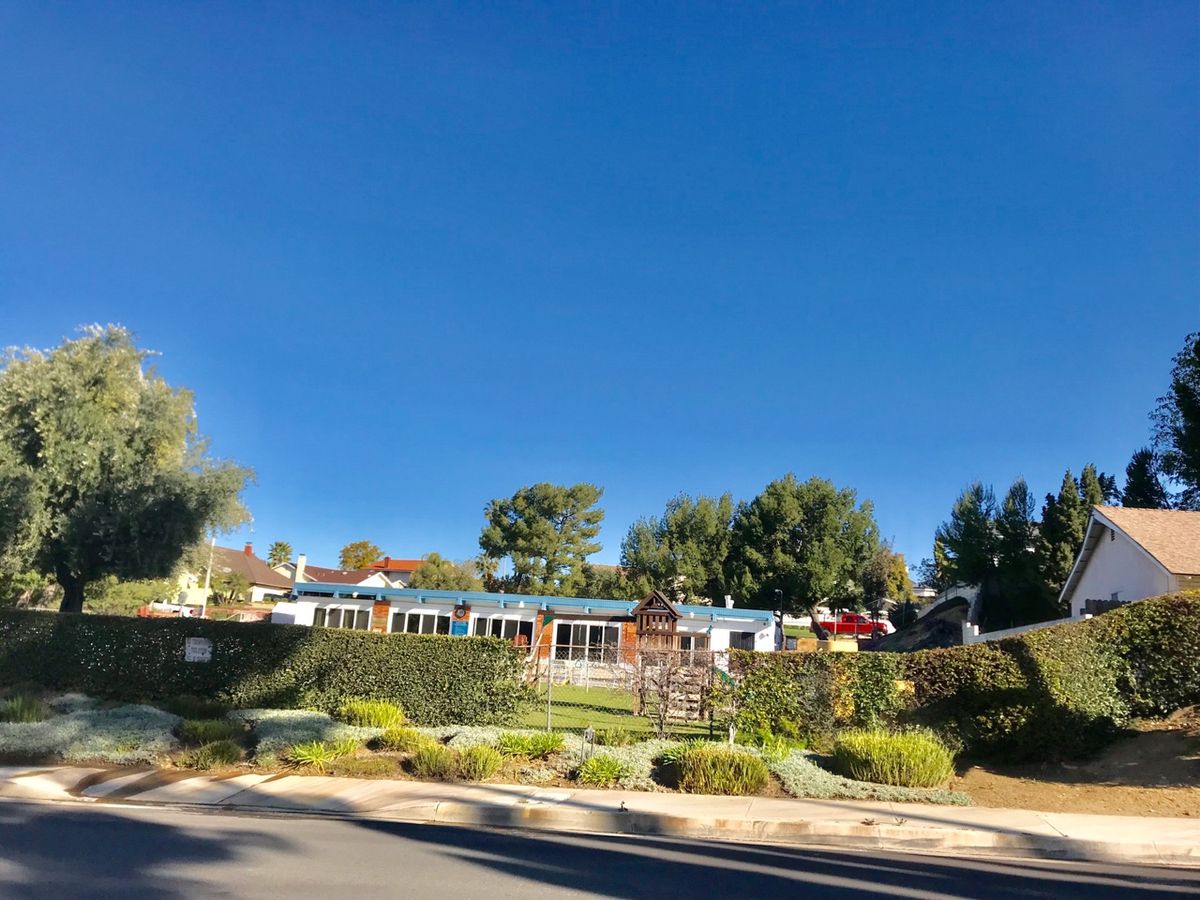 A scenic view of a building surrounded by lush gardens and trees under a clear blue sky.