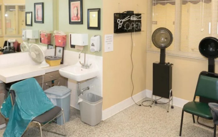 A cozy salon interior featuring a hair dryer, sink, and seating area with wall decorations.