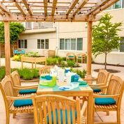 A cozy outdoor patio area with a wooden pergola, featuring a table and chairs set for dining amidst a garden setting.