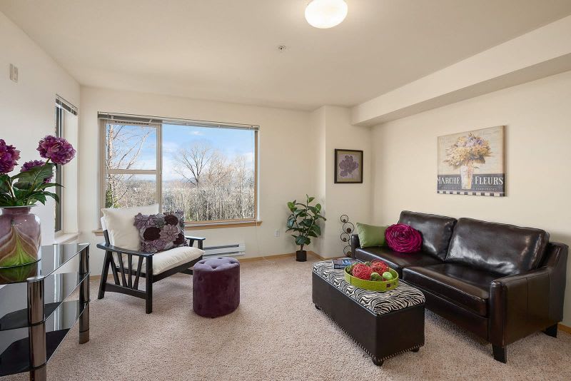A cozy living room with a sofa, armchair, and large window providing natural light.