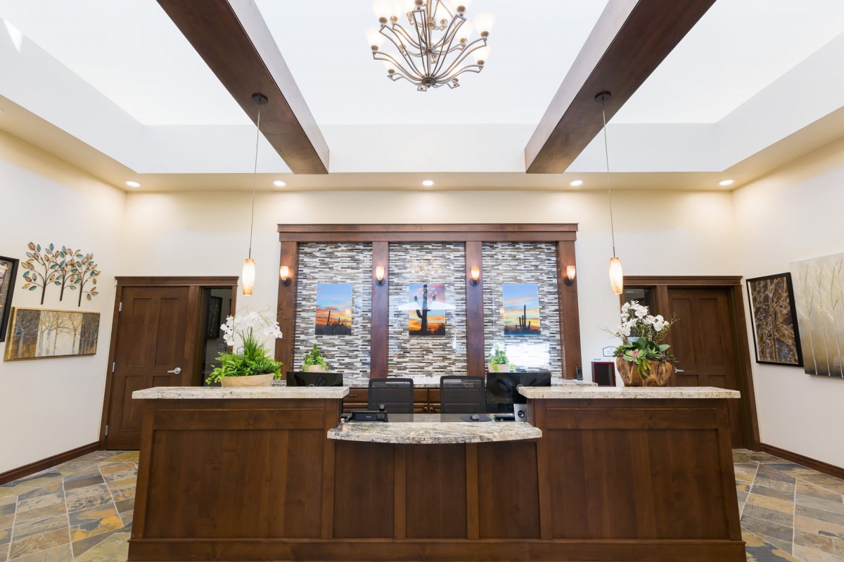 A well-lit hotel reception area featuring a wooden desk, decorative lighting, and elegant interior design.