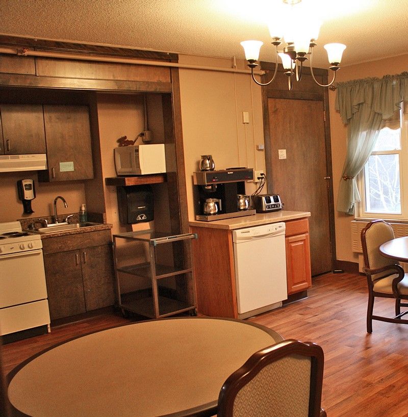 A cozy kitchen with wooden cabinets, a dining table and chairs, featuring various appliances and a chandelier.