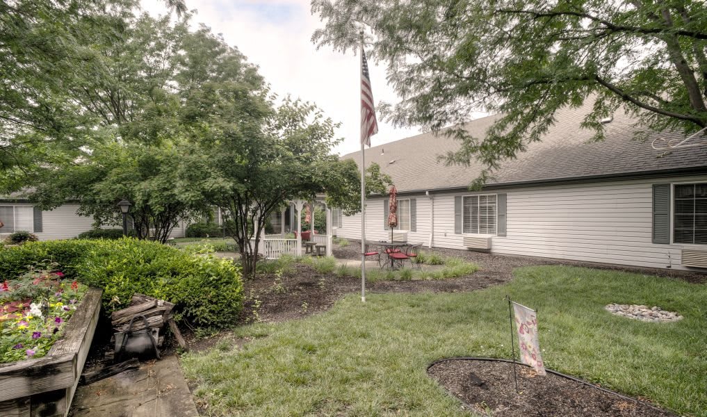 A suburban home with a well-maintained garden, featuring a flagpole and surrounded by trees.