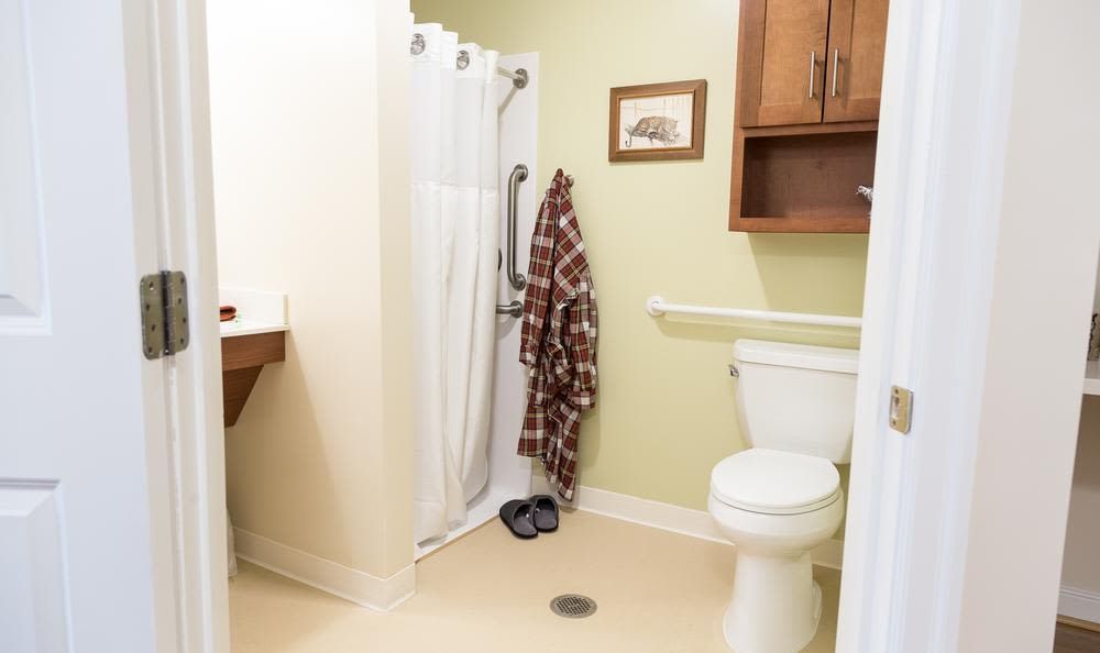 A cozy bathroom with a shower, toilet, robe hanging on a hook, and slippers on the floor.