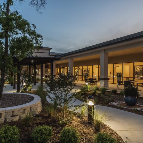 A modern building with outdoor lights illuminating a landscaped patio area during the evening.