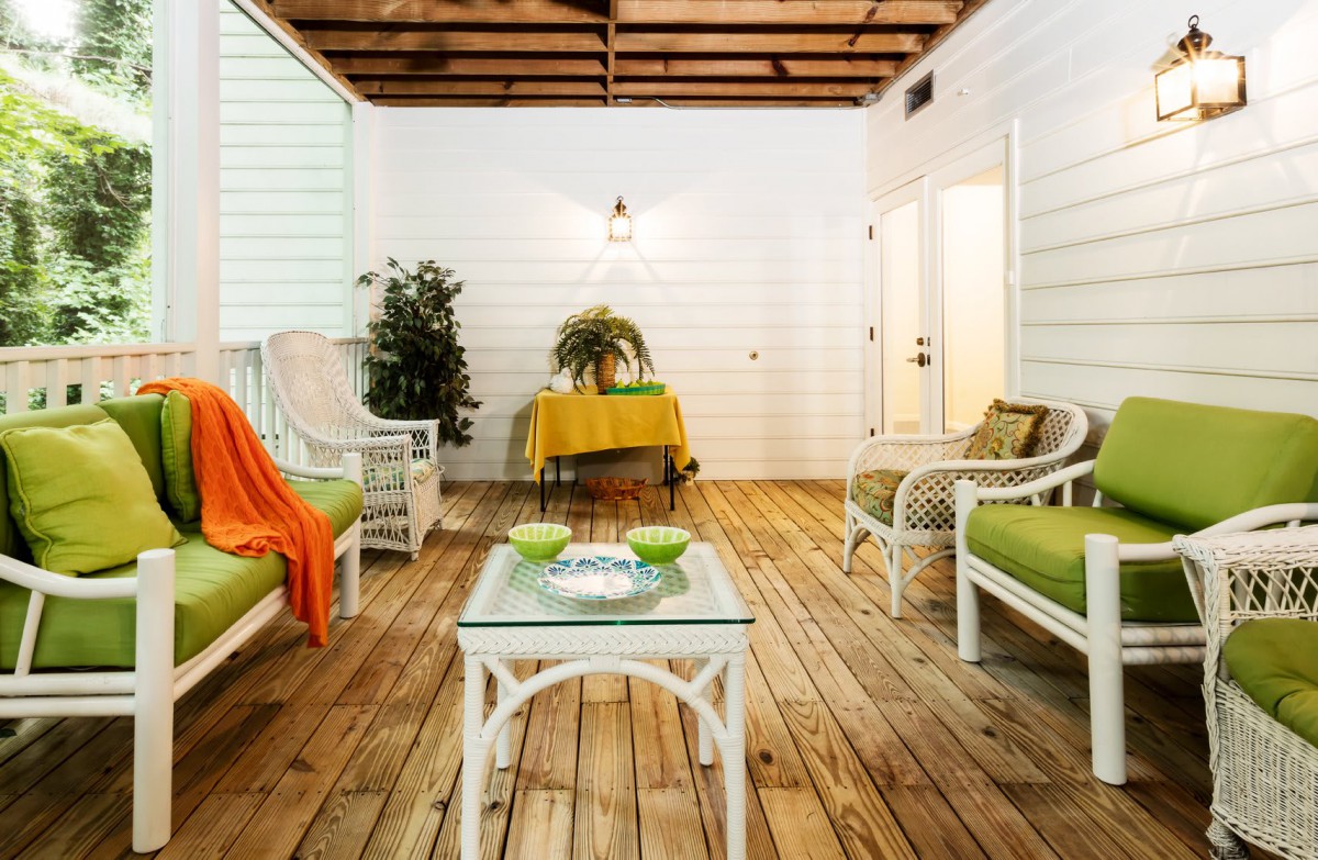 A cozy outdoor patio with rattan furniture and green cushions, complemented by a warm orange blanket and potted plants.
